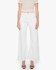 A person wears The Lemon Twist Skimp by Mother—high-rise, wide-leg cotton-blend pants—paired with a beige cropped top and black open-toe heels, standing against a white background.