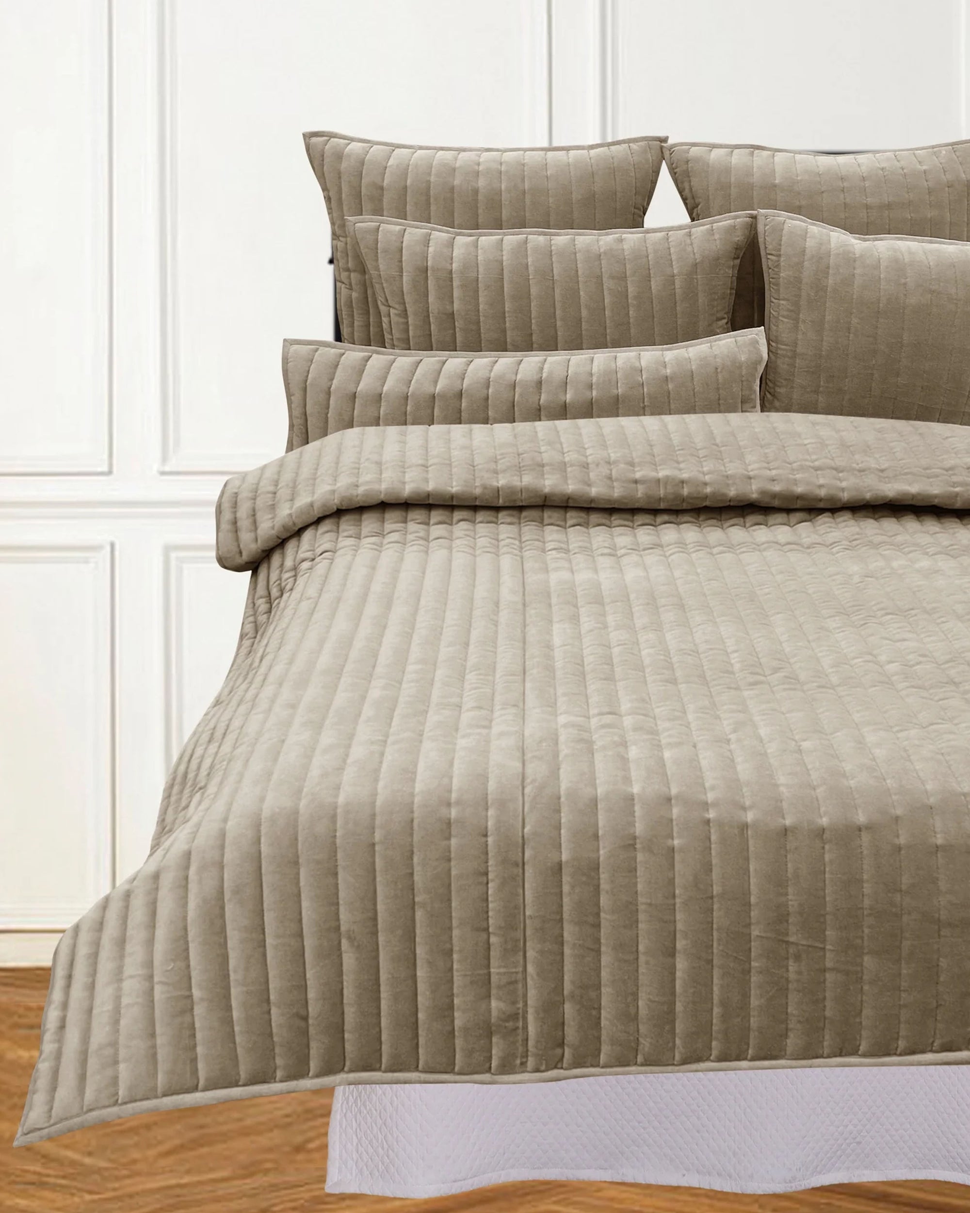 A neatly made bed features the Avasa Bedding Lennon Quilt Beige King with matching pillows, set against a white paneled wall and a glimpse of a wooden floor.