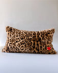 Leopard print faux fur lumbar pillow with red heart patch by Faire Muse on a light background.
