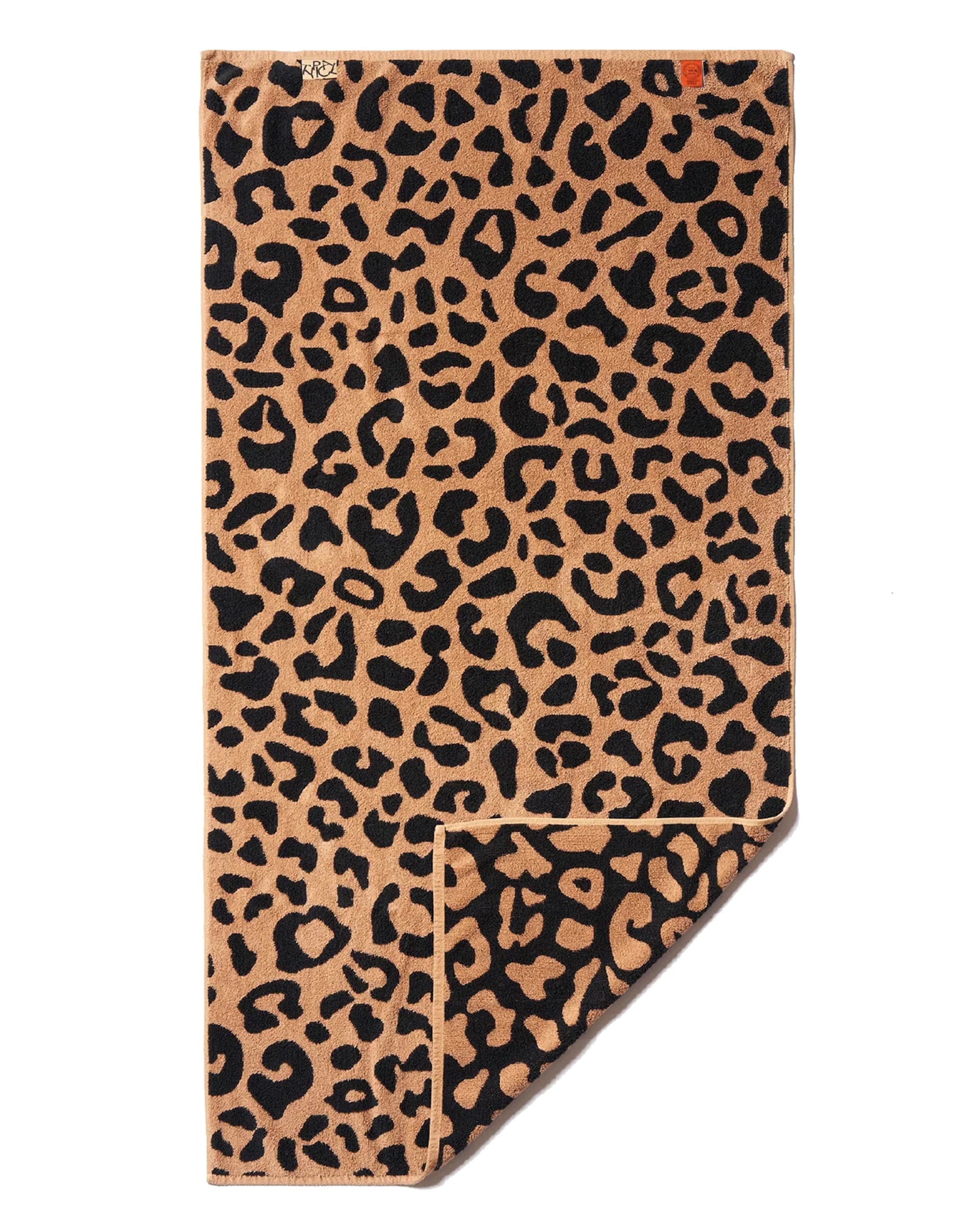 The Typical Wild Leopard Bath Towel features a bold black leopard print on a tan background, with one corner folded to show the underside.
