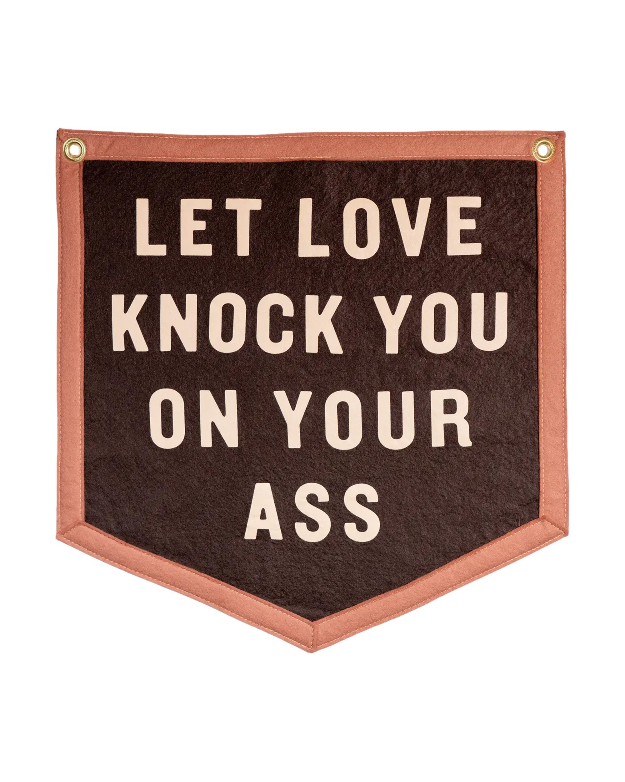 The Faire Let Love Knock You Camp Flag features a brown banner with a pink border, gold grommets, and bold cream letters reading "LET LOVE KNOCK YOU ON YOUR ASS"—relationship advice reminiscent of a Jason Isbell lyric.