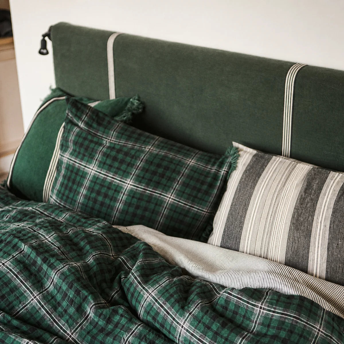 Jack Check Sham from Libeco Home on a bed with a green striped headboard for a fresh, classic bedroom look.