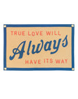The Oxford Pennant "True Love Will Always Have It's Way" flag features a gold background, blue border, red and blue lettering, felt wall hanging style, and four gold grommets—an homage to John Prine.