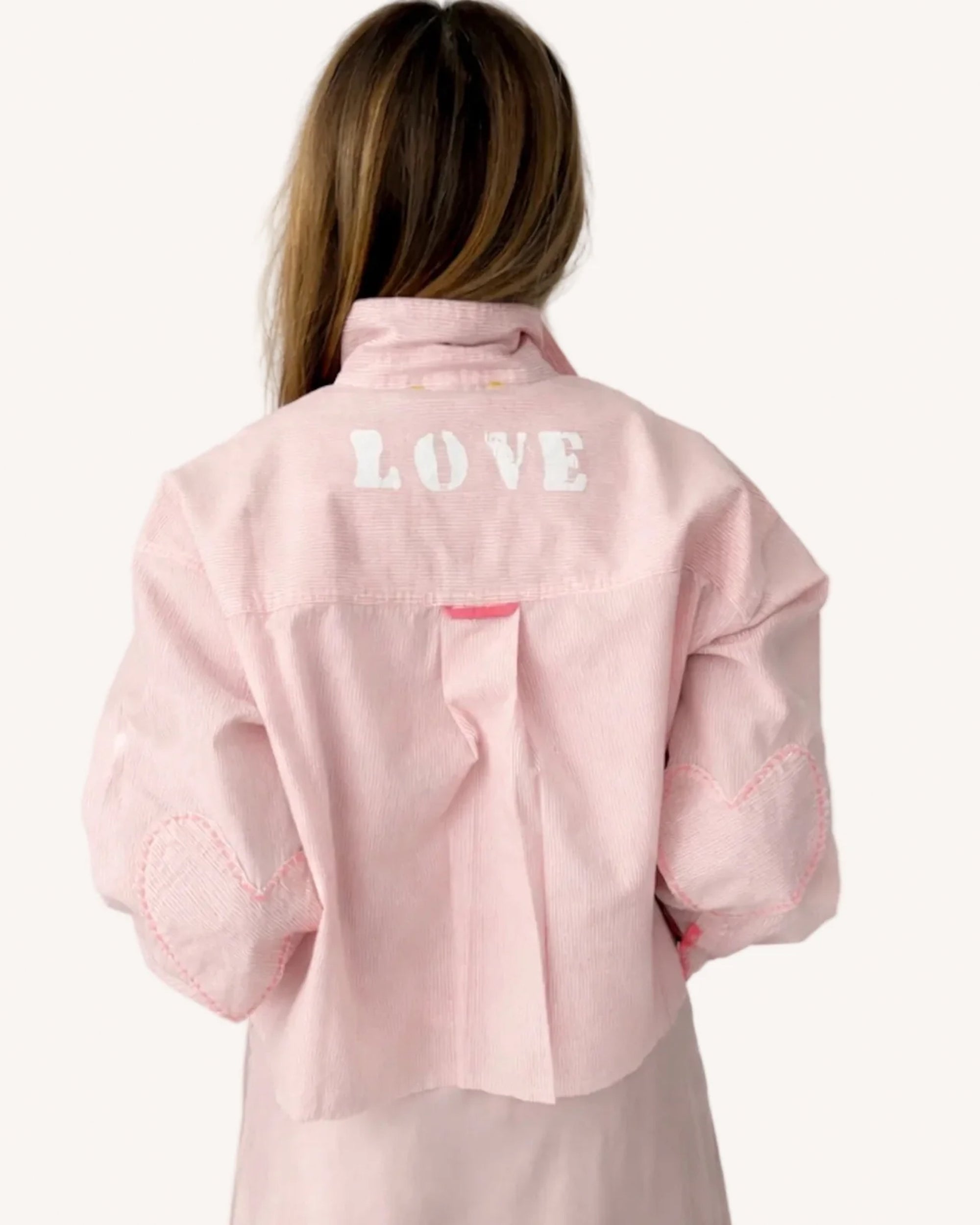 Pink jacket layered over a Kerri Rosenthal Tia Love Stripe Shirt, seen from behind in a casual, modern setting.