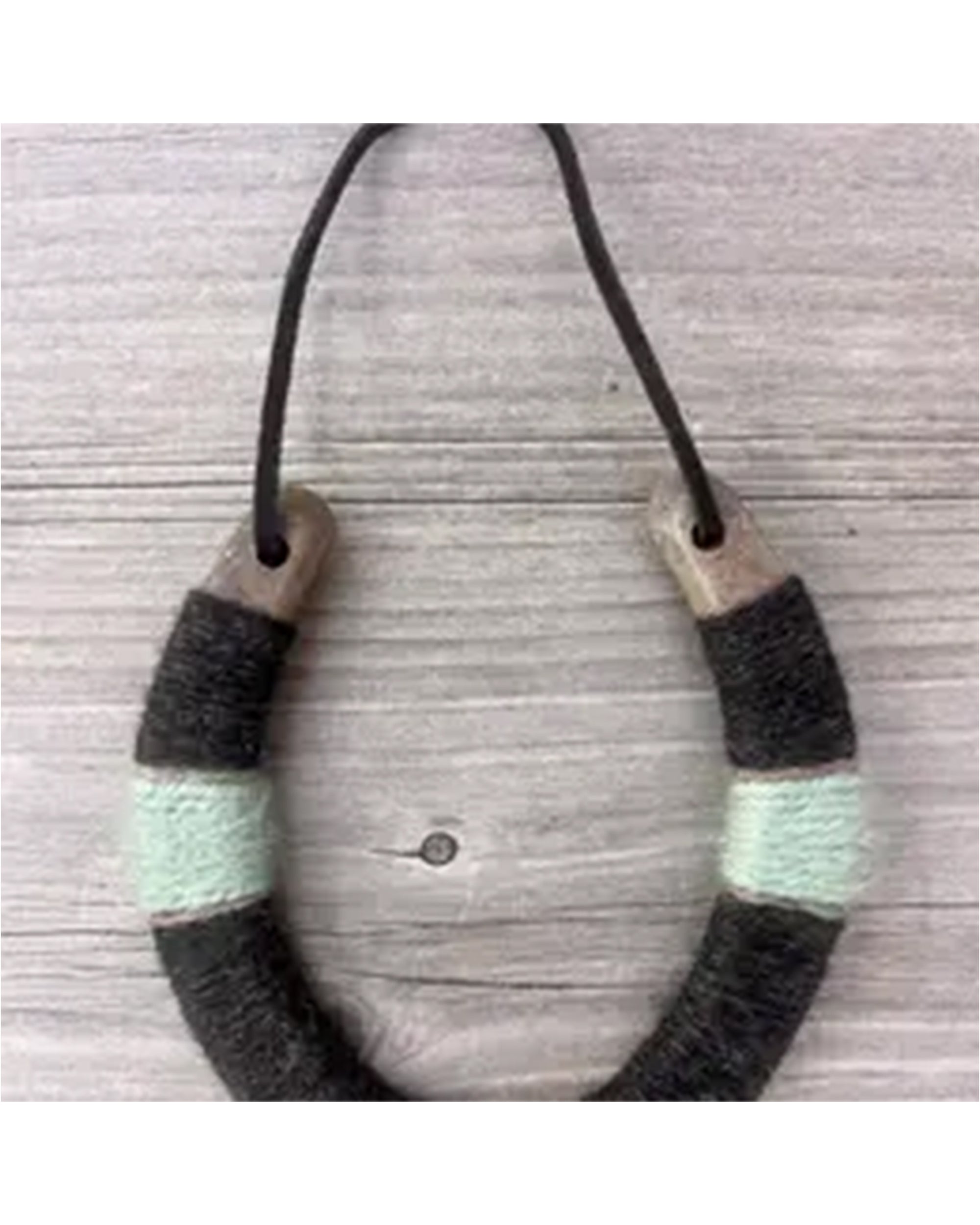 The Faire Lucky Horseshoe is a handmade necklace with a U-shaped pendant, crafted from upcycled horseshoes and wrapped in dark gray and mint green thread—an eco-friendly housewarming gift on a thin black cord.
