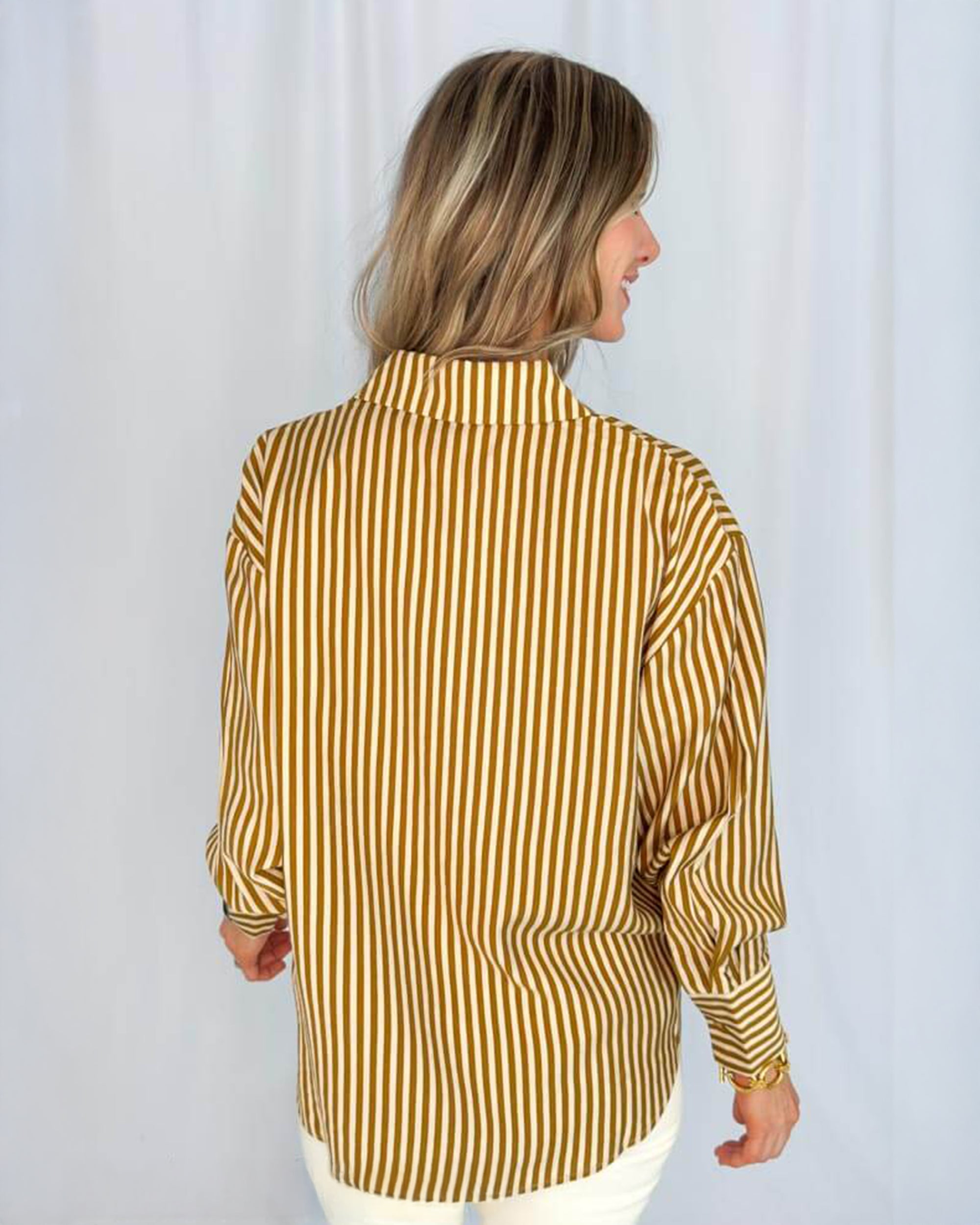 A person with blonde hair, seen from the back, wears the SUNCOO Lynsha Blouse—a loose-fitting, long sleeve collared top with vertical mustard yellow and white stripes—against a plain white background.