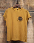 The Made Worn "MadeWorn Records" vintage unisex pocket tee in mustard yellow distressed cotton features a circular logo on the chest pocket. Handmade in Los Angeles, it’s shown on a wooden hanger with a rustic wood background.