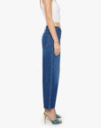 Woman stands sideways against a white background, wearing a white crop top, Mother’s The Delinquent Ankle high-waisted denim jeans, teal open-toe heeled sandals, and a bracelet.