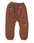 MadeWorn P.E. Sweatpants by Made Worn: heavyweight brown French terry joggers with elastic cuffs, colorful paint splatters, a round "MADE WORN 1971 ARTIST SH*T" patch on the left thigh, and a yellow smiley face patch on the right knee. Unisex fit.