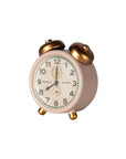 The Maileg Alarm Clock by Maileg is a small vintage-style pink metal clock with gold bells and legs, displaying 12:00, set against a white background.