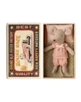 The Maileg Little Sister Mouse by Maileg wears pink gingham pajamas and lies on a blanket in an open matchbox. The box lid features a vintage race car and the words “Mouse Race” and “Best Quality.”.