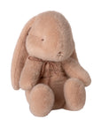 The Maileg Bunny Plush is a soft, light brown stuffed bunny with floppy ears and simple facial features, sitting upright and wearing a thin brown ribbon around its neck.