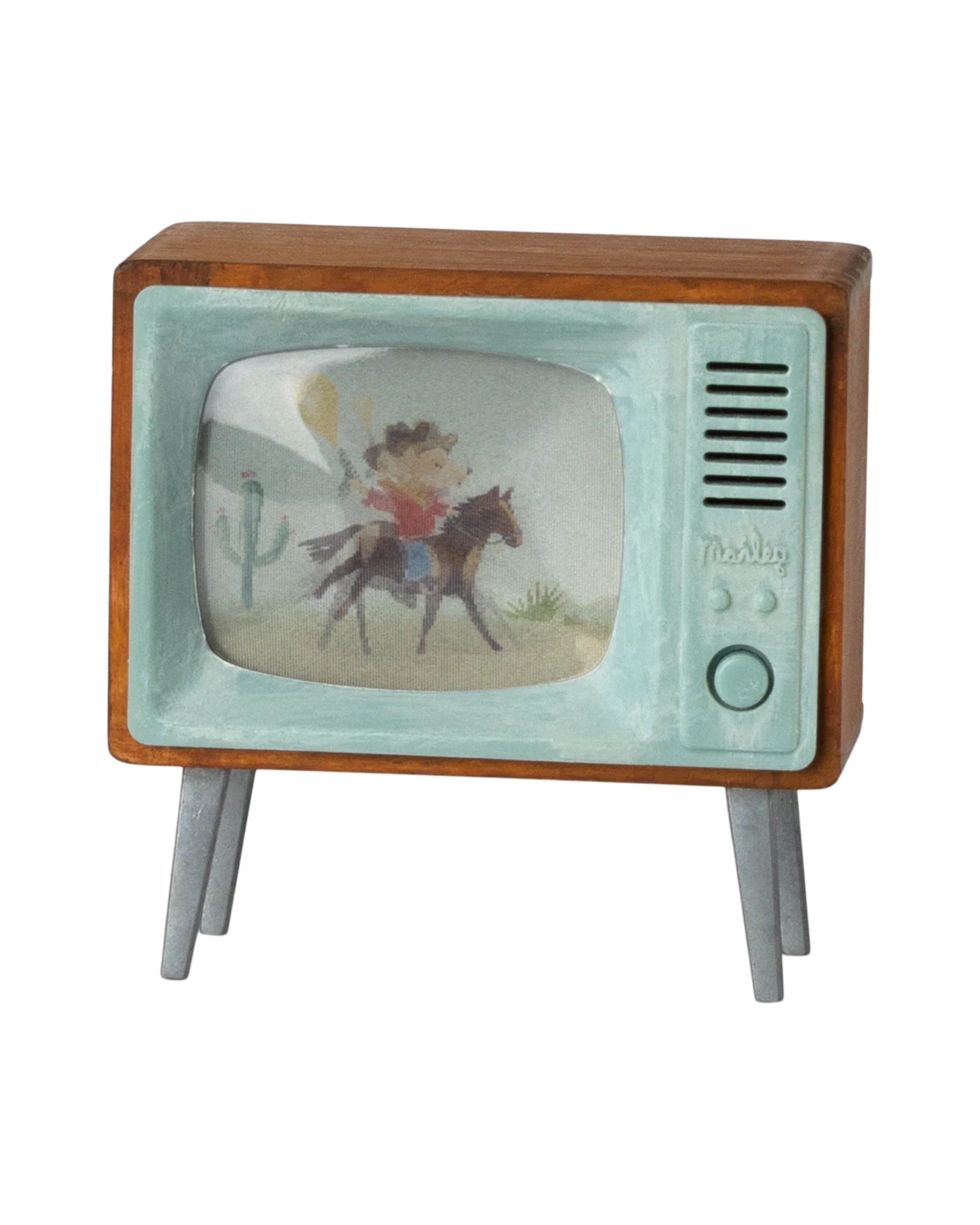 The Maileg Television by Maileg is a small, retro-style TV with a wood frame and metal legs, featuring a cartoon cowboy on horseback with a cactus in the background displayed on its screen.