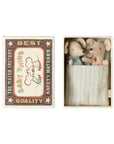 Maileg Baby Twins Matchbox by Maileg features two small baby mice in blue and pink outfits, cozily wrapped in a striped blanket inside a matchbox bed with "The Match Factory Best Quality Baby Twins Safety Matches" and twin mouse artwork on the lid.