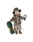 The Maileg Wildlife Guide Mouse by Maileg wears a plaid shirt, hat, and shorts, and is ready for adventure—holding a magnifying glass in one hand and a rolled-up sleeping bag in the other.