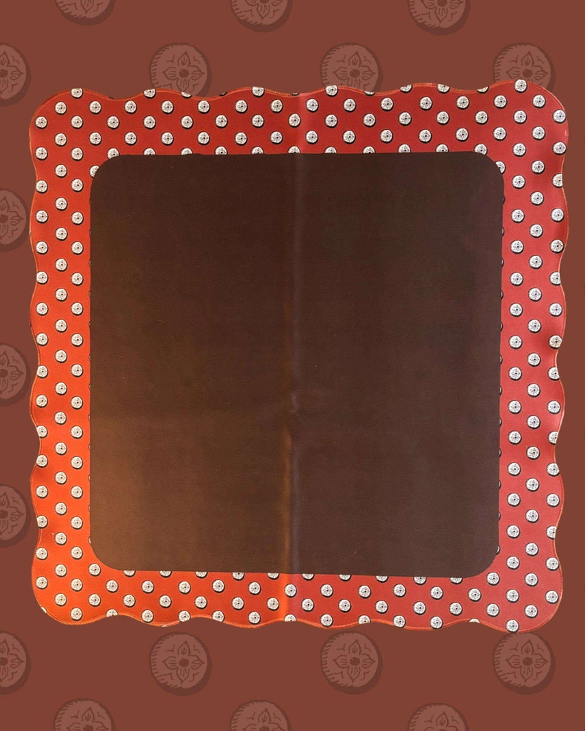 The Wild West Mahjong Mat ONLY by Faire features a rectangular, blank surface with red, scalloped, wavy borders adorned with white polka dots and a reddish-brown background patterned with repeating compass-like designs.