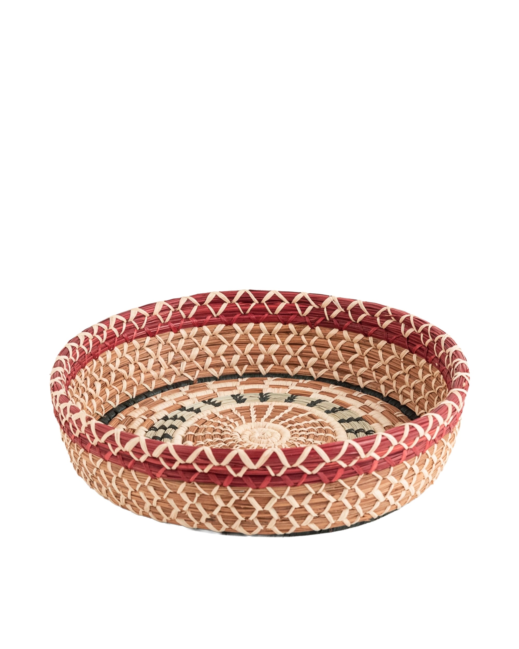 The Manuela Basket by Faire is a woven, round Guatemalan basket with a patterned design in natural, red, and dark green hand-dyed raffia. It features short sides, a flat base, and is shown on a white background.