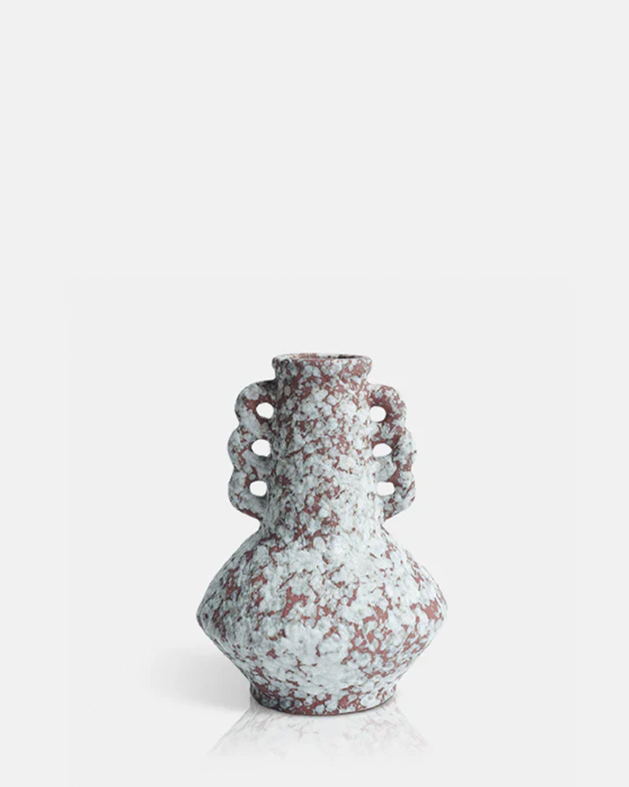 The AA-M9-001 Marilla Vase by Abigail Ahern is a decorative ceramic piece with a rounded body, narrow neck, and two ornate handles featuring circular cutouts. Its marbled red and white surface stands out against a plain white background.