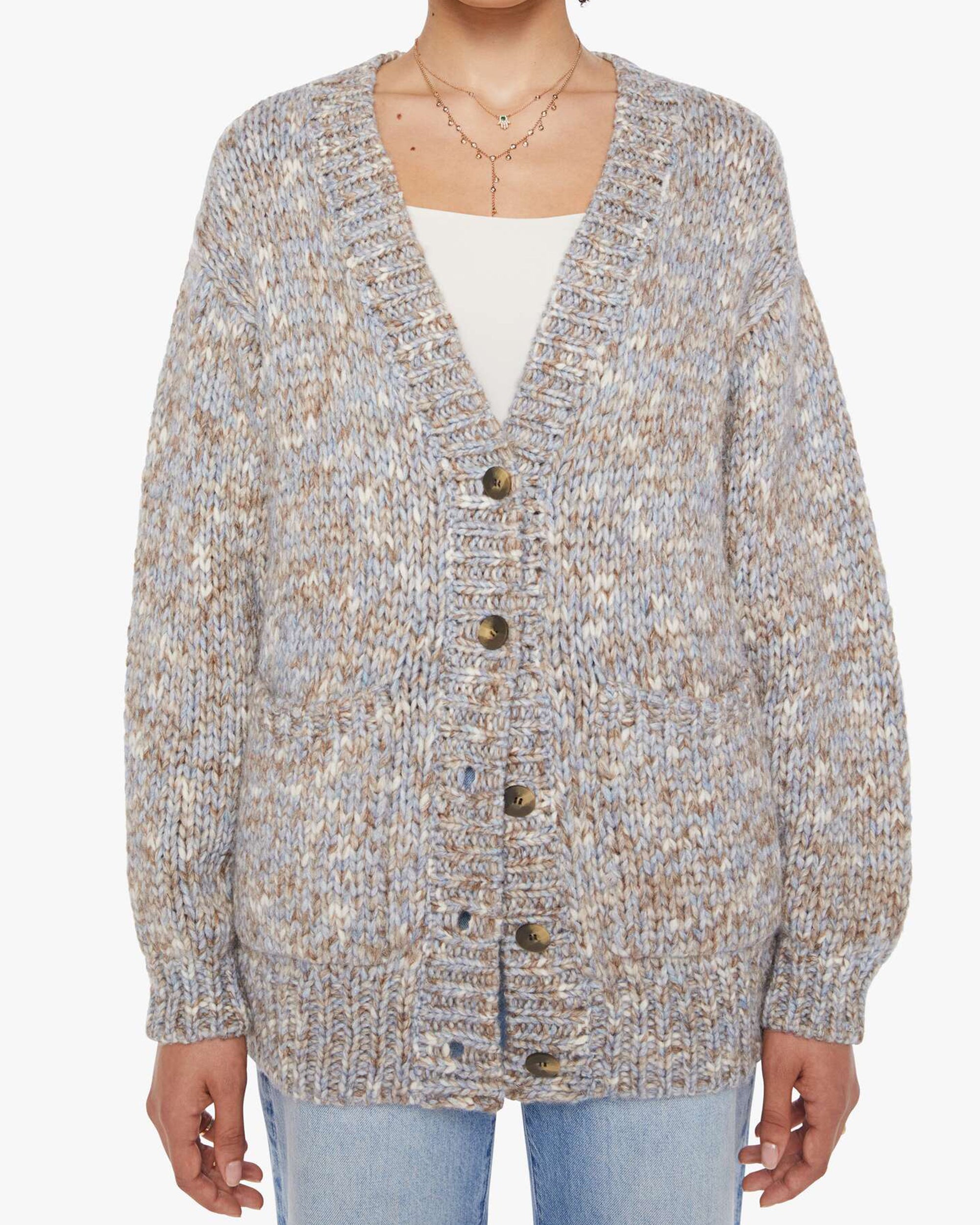 A person wears the Xirena Marvin Sweater, a chunky knit oversized V-neck cardigan in beige, blue, and white baby alpaca yarn. It's buttoned over a white top and light blue jeans, with ribbed cuffs and hem.
