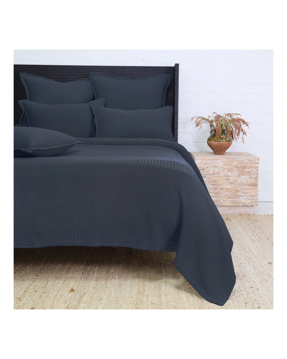 Dark gray Chatham Matelasse King bedding by Pom Pom, layered with pillows beside a plant in a cozy bedroom setting.