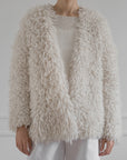 A person wearing the cream Medusa Cardigan Coat by LATIERRA over a knitted sweater and white pants stands against a light background—embodying sustainable luxury and cozy style.