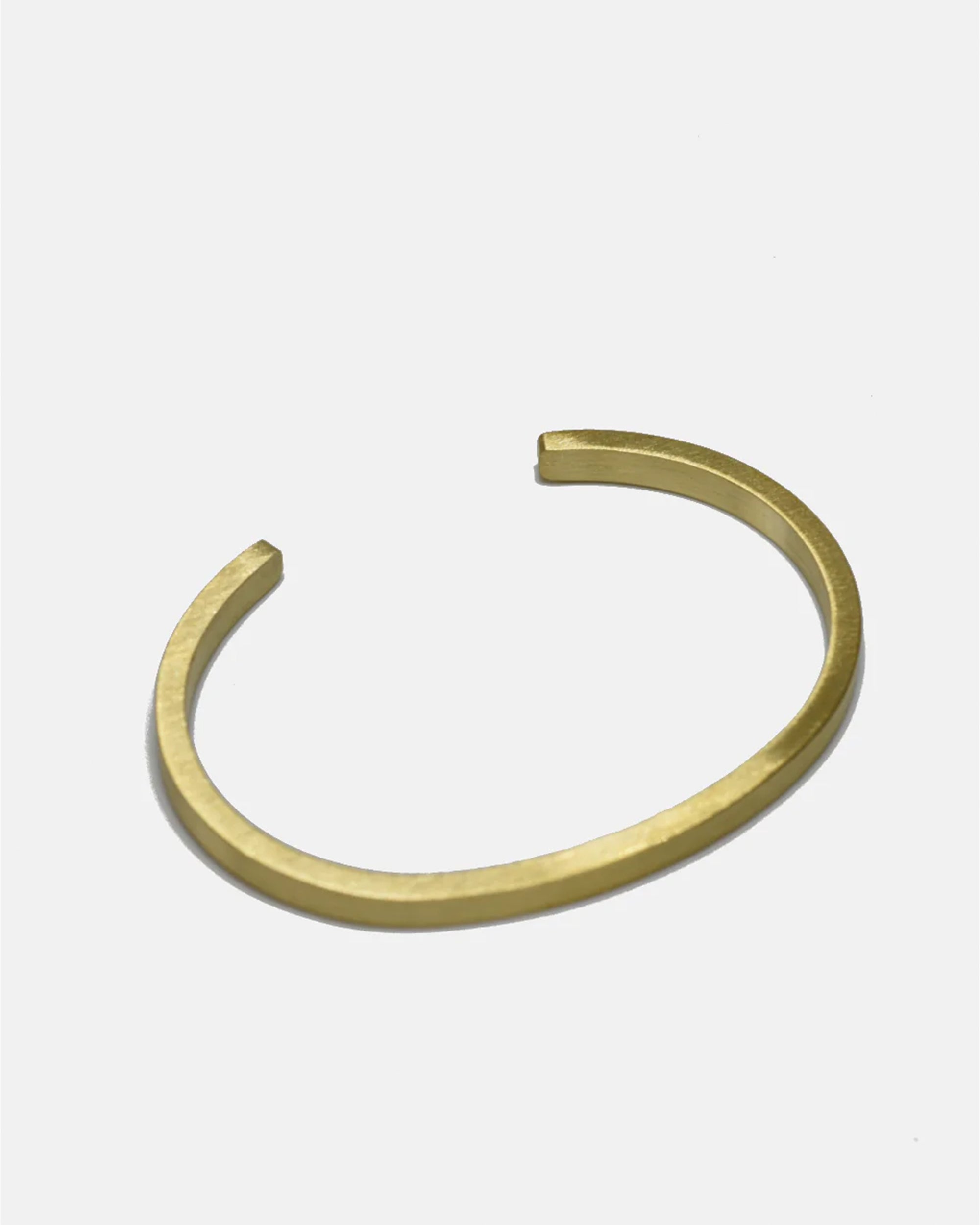The Curated Basics MENS Flat Cuff is a minimalist gold brass bracelet with a 5mm width and smooth matte finish, open-ended to elegantly wrap the wrist. Shown on a plain white background.