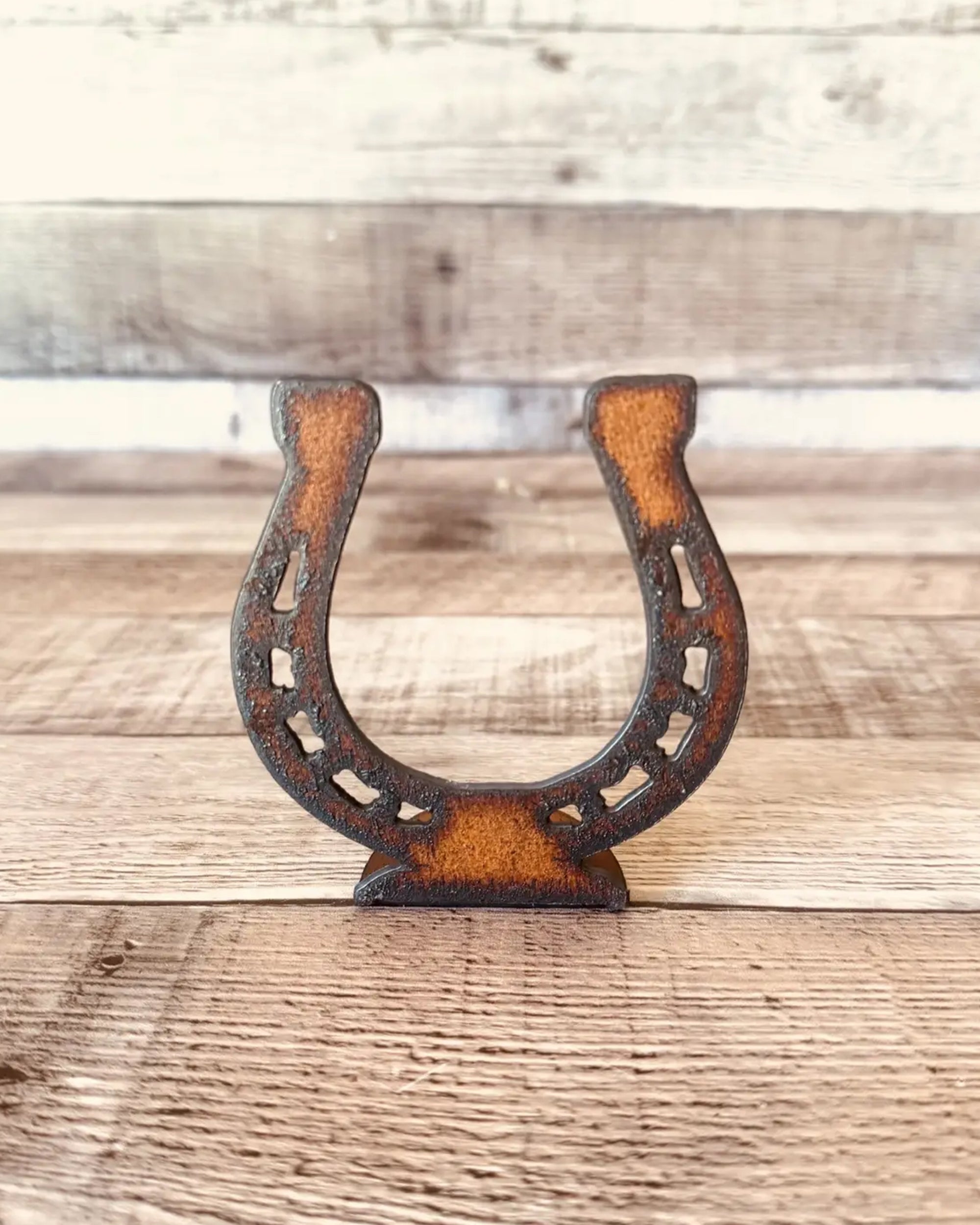 The Faire Horseshoe Rustic Western Doodad is a brown metal tabletop figurine with a vintage look, standing upright on wood for charming rustic decor.