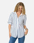 A woman with shoulder-length blonde hair wears the Kerri Rosenthal Mia Mr Sharpie Stripe Shirt, featuring vertical navy stripes, paired with blue jeans and layered jewelry, smiling as she looks down against a white background.
