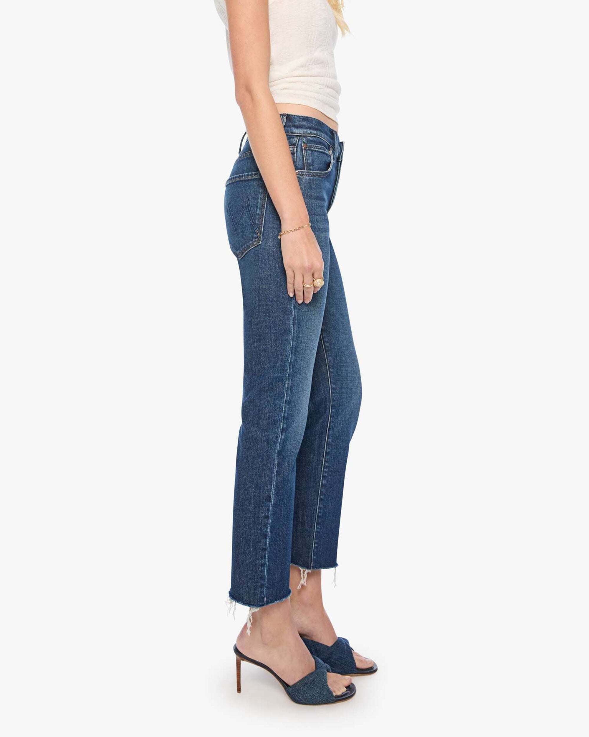 Mother The Mid Rise Hiker Hover fray jeans in blue denim styled with a white top and sandals against a white backdrop.