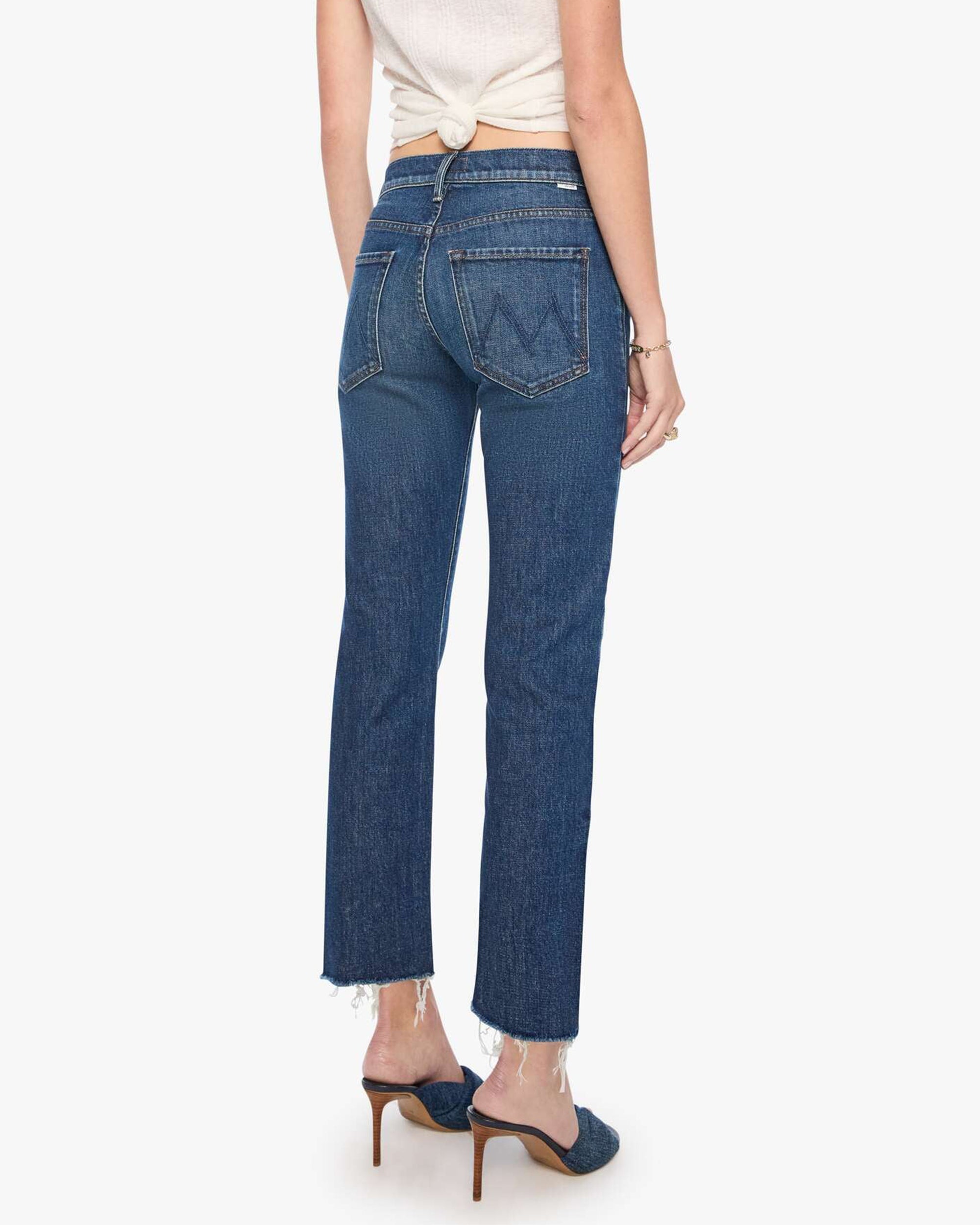 Mother’s The Mid Rise Hiker Hover fray jeans in blue denim, styled with heels and a knotted white top, back view.