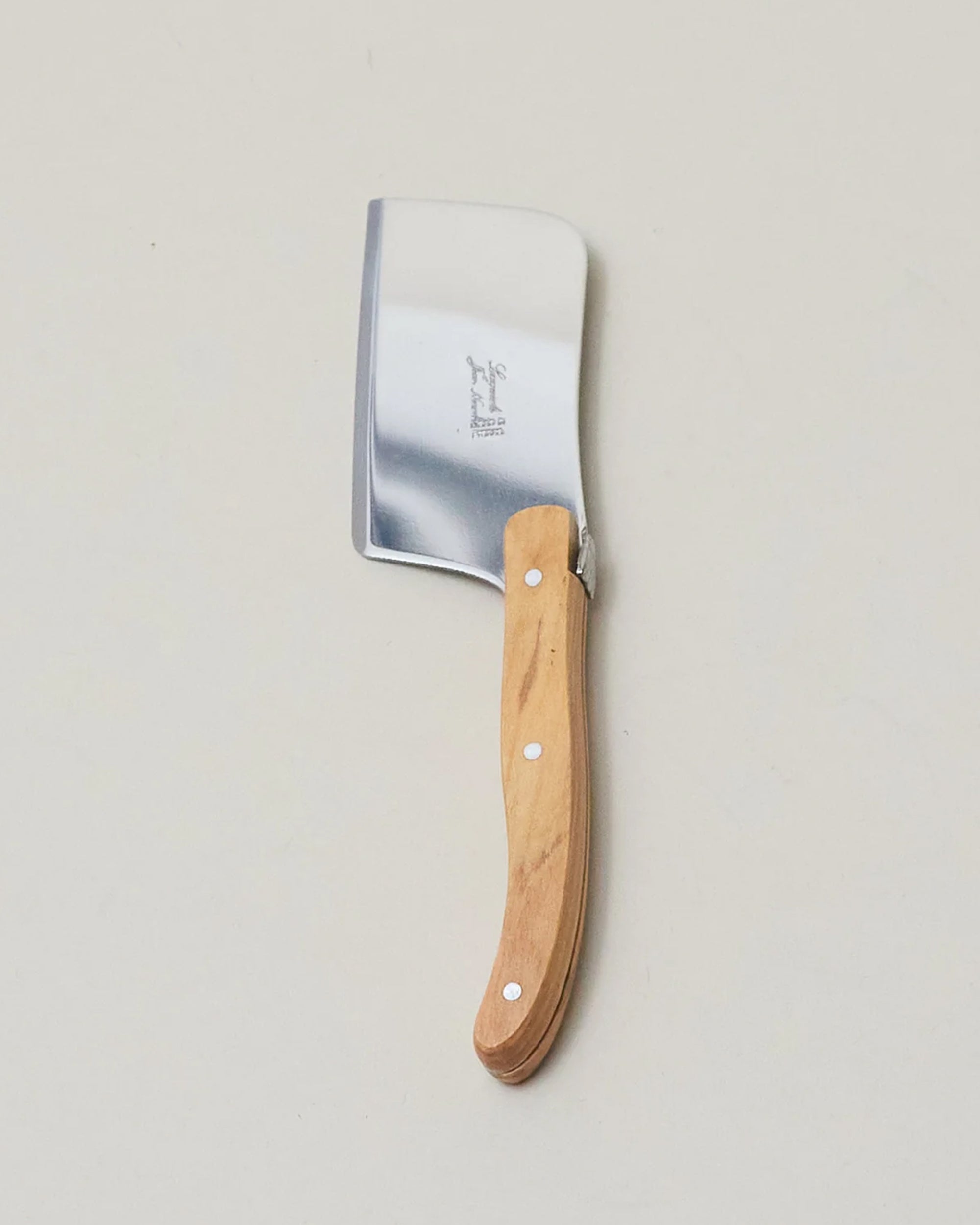 The Laguiole Mini Cutter by Be Home, featuring a shiny rectangular blade and a light brown wooden handle that highlights French craftsmanship, rests on a plain light-colored surface.