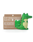 The Faire Alligator Embroidery Kit includes a cardboard package with an illustrated pattern and lets you create a green stuffed alligator doll with embroidered yellow details.