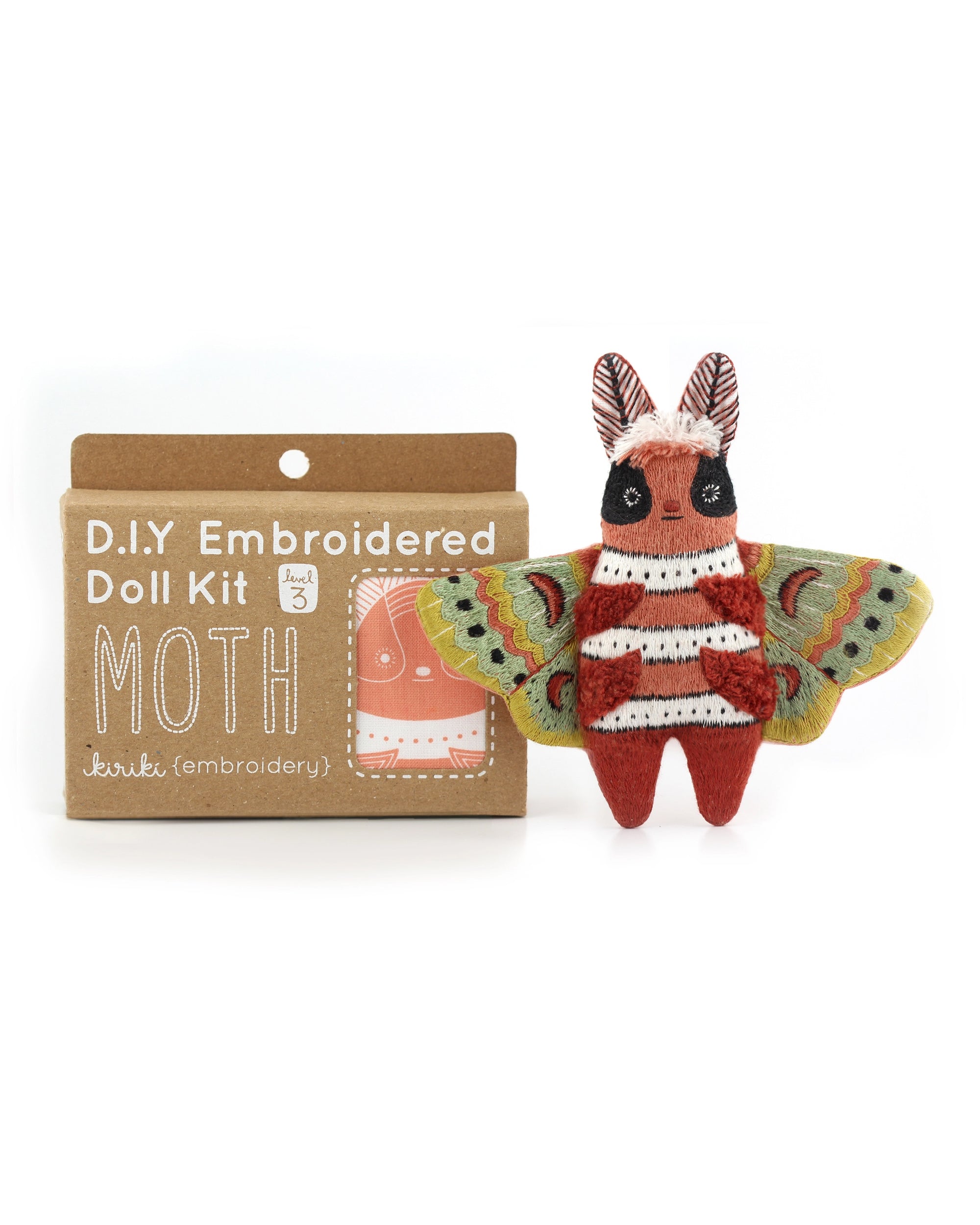 The Faire Moth Embroidery Kit is shown beside a completed, colorful moth doll. Ideal for beginners, it comes in a brown box with white text and includes an unassembled doll embroidery pattern.