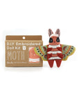 The Faire Moth Embroidery Kit is shown beside a completed, colorful moth doll. Ideal for beginners, it comes in a brown box with white text and includes an unassembled doll embroidery pattern.