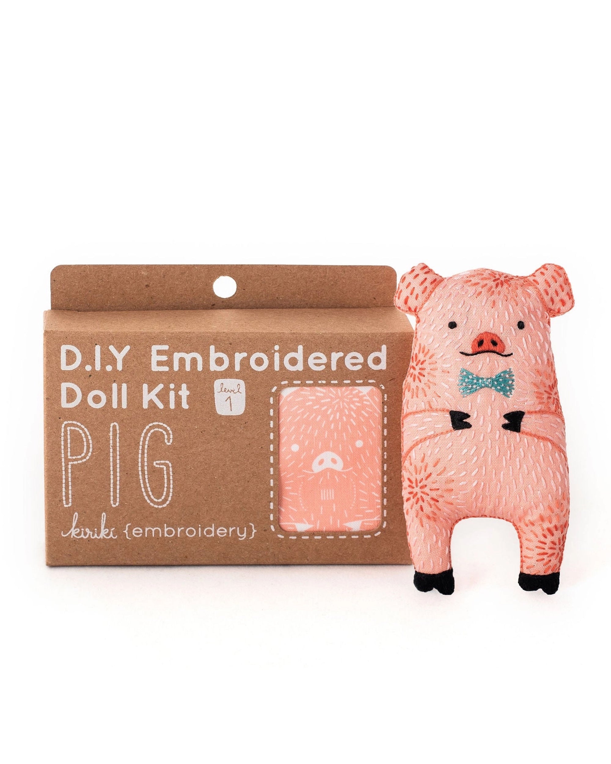 The Faire Pig Embroidery Kit is a level 1 beginner set with materials to craft a pink pig plushie with a blue bow tie. The packaging shows an illustration of the finished pig and highlights its suitability for embroidery novices.