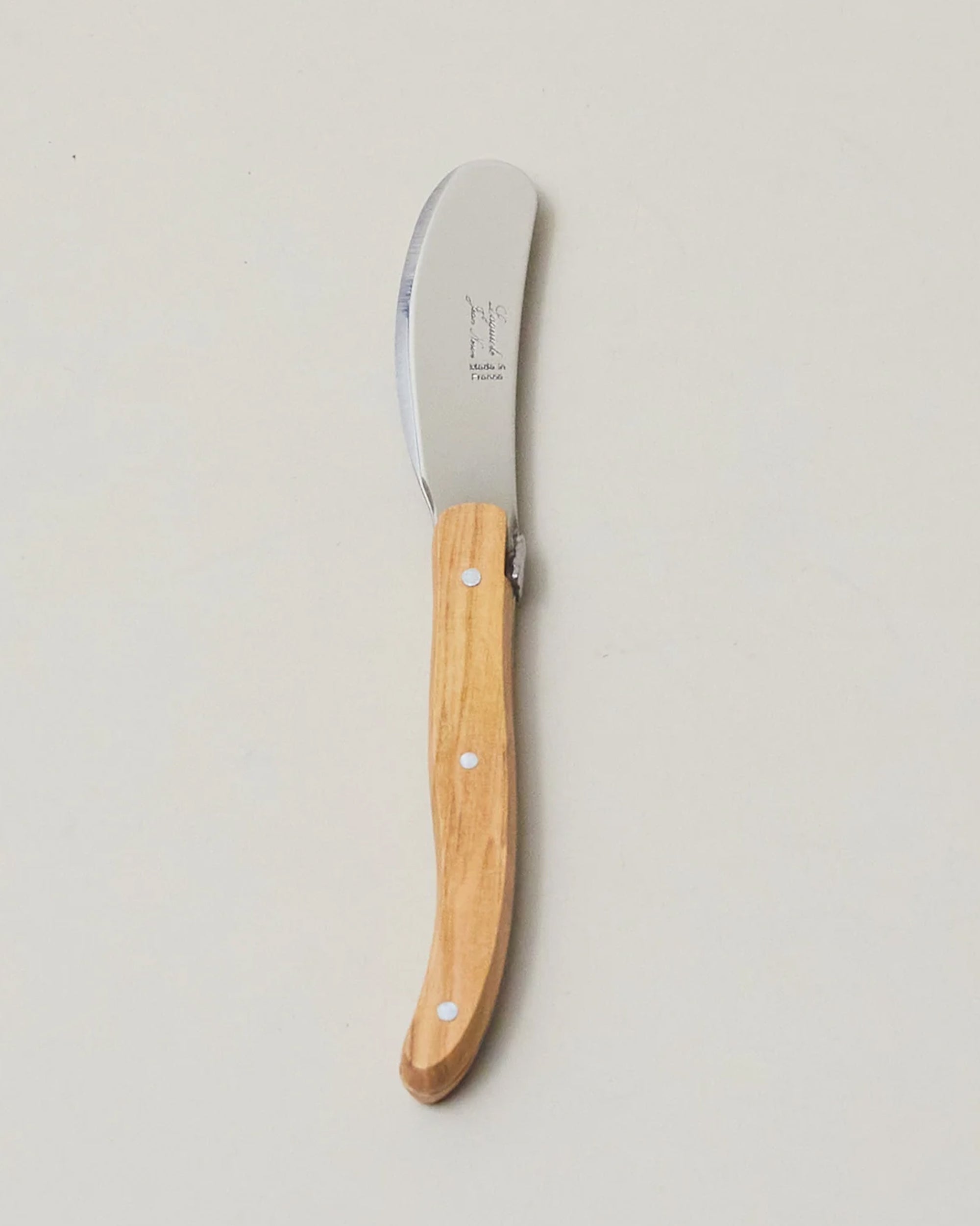 The Be Home Laguiole Mini Spreader, featuring a wooden handle and stainless steel blade with French craftsmanship, rests on a plain light-colored surface.