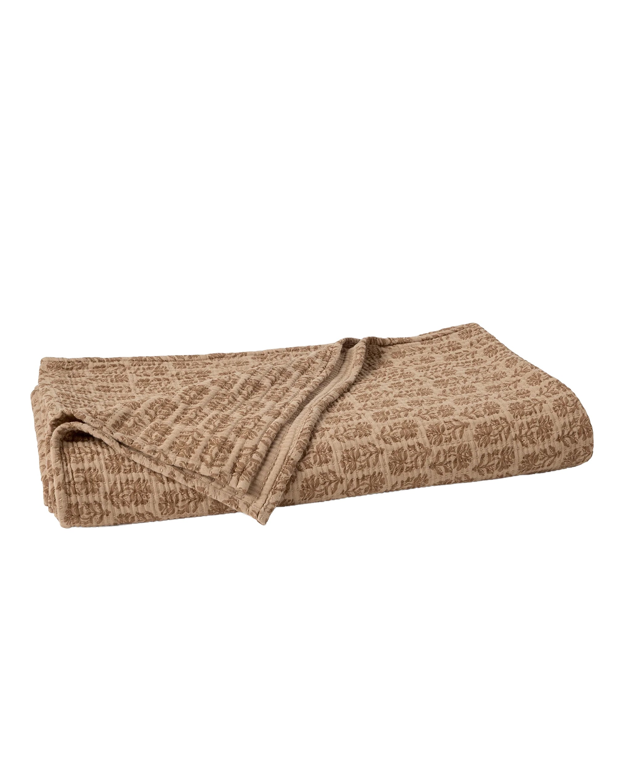 The Mirada Matelasse Blanket by Coyuchi Inc, shown folded on a white background, features light brown organic cotton and a subtle, repeating jacquard matelassé pattern.