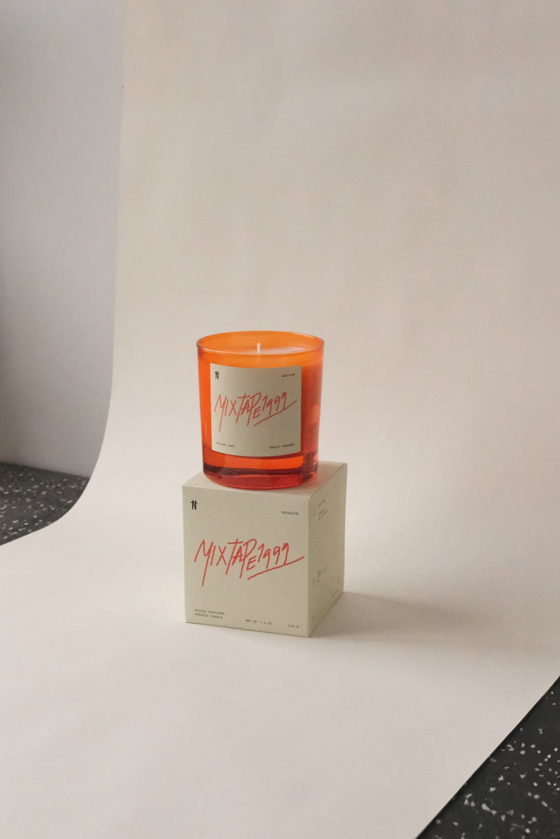 A Nosedive Candle by Faire sits on a matching box, both on a white surface with a neutral background, evoking 70's music nostalgia.