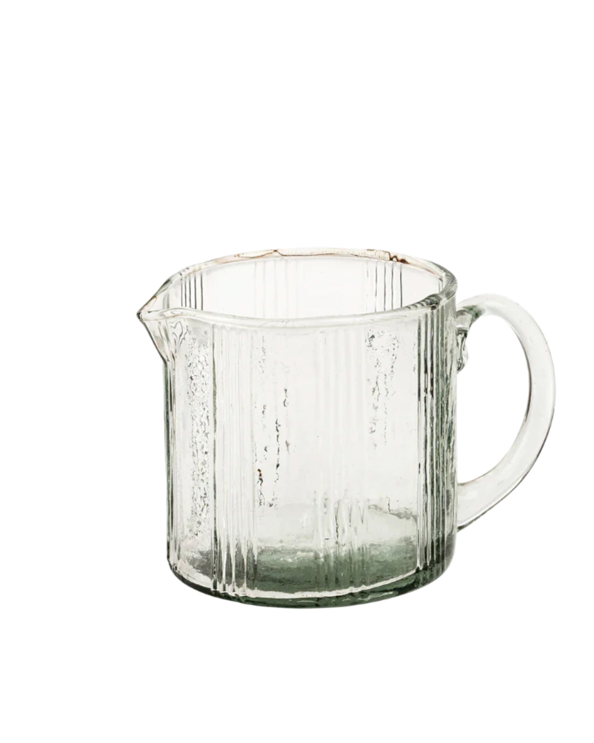 The Indaba 4-7026 Monaco Petit Pitcher is a clear artisanal glass measuring cup with vertical ribbed texture, a rounded handle, and a spout for pouring, shown against a plain white background.