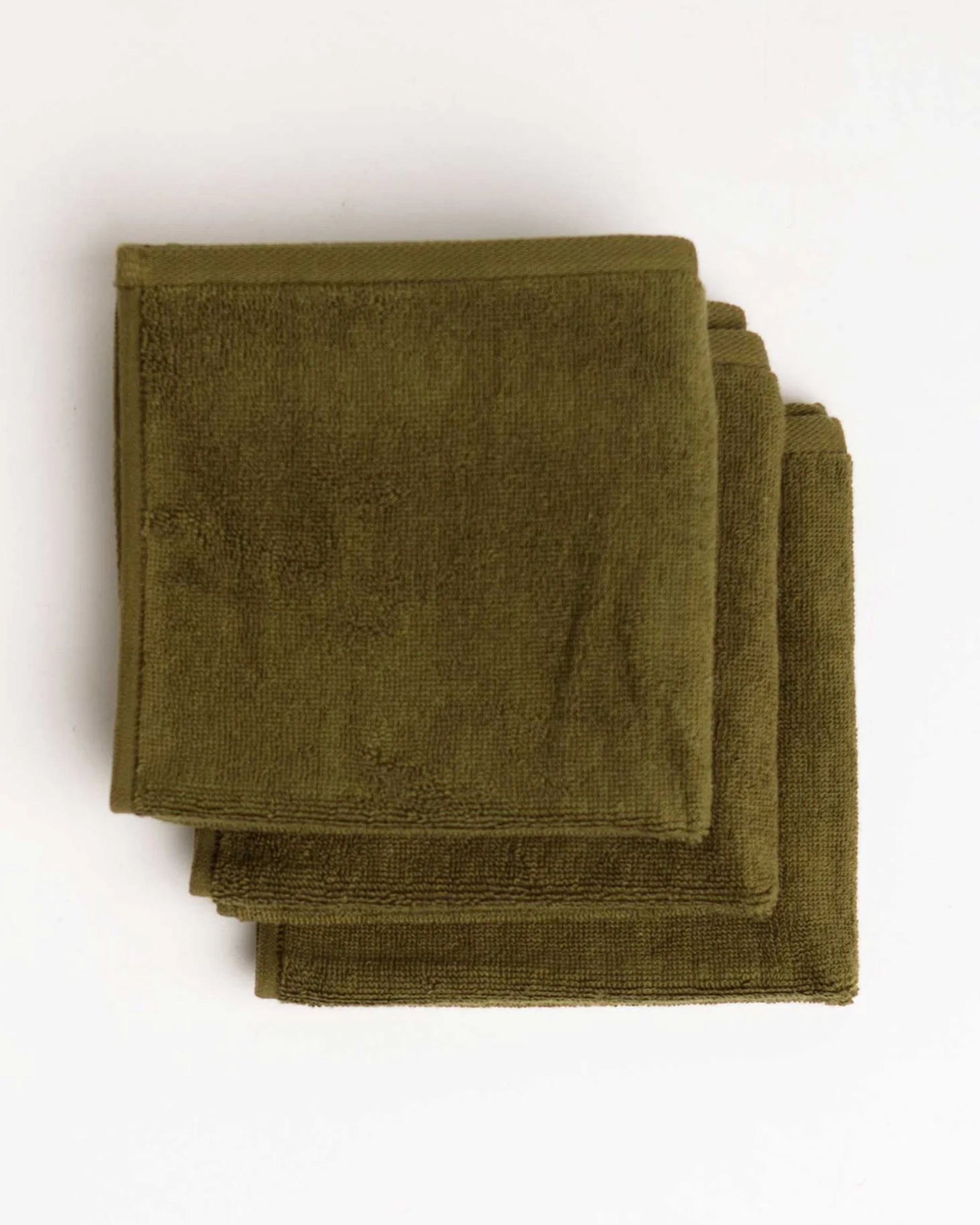 Three Moss Green Face Towels by Typical are neatly stacked on a white background, highlighting their stylish and essential design.
