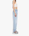 A woman in profile wears the Mother The Dodger Button Hover Cuff light blue slouchy jeans with loose straight legs and cuffs, styled with a white sleeveless crop top and blue high-heeled sandals against a plain background.