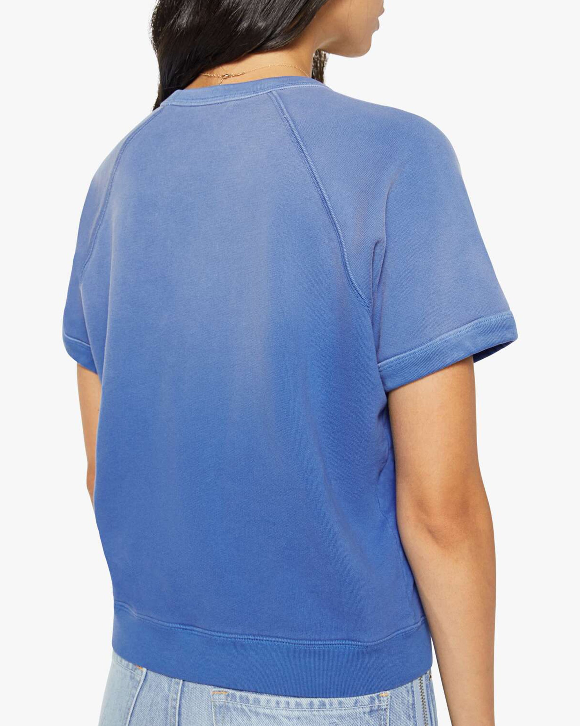 A woman with long dark hair is seen from the back, wearing Mother’s The Short Sleeve Concert Tee and light blue jeans against a plain white background.
