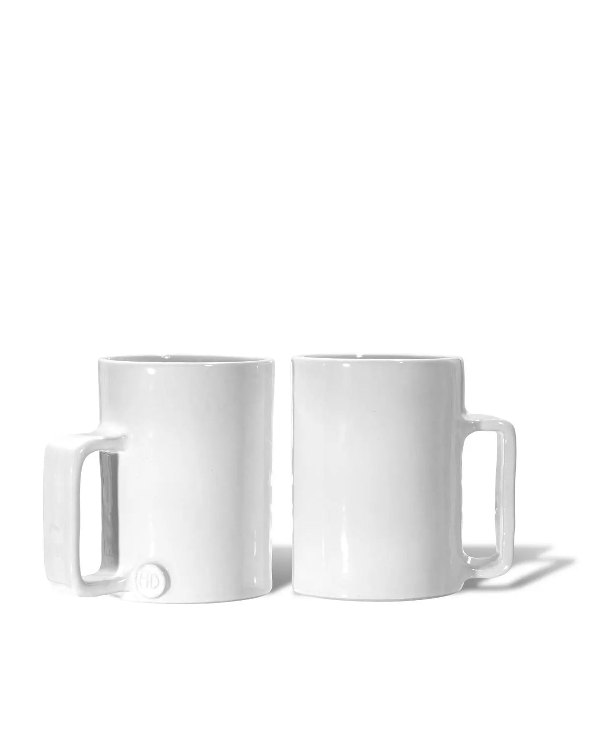 Two Montes Doggett 5429 Mug No. 429 white ceramic mugs are side by side on a white background; the left has a rectangular handle with an embossed circular logo, while the right features a standard handle.