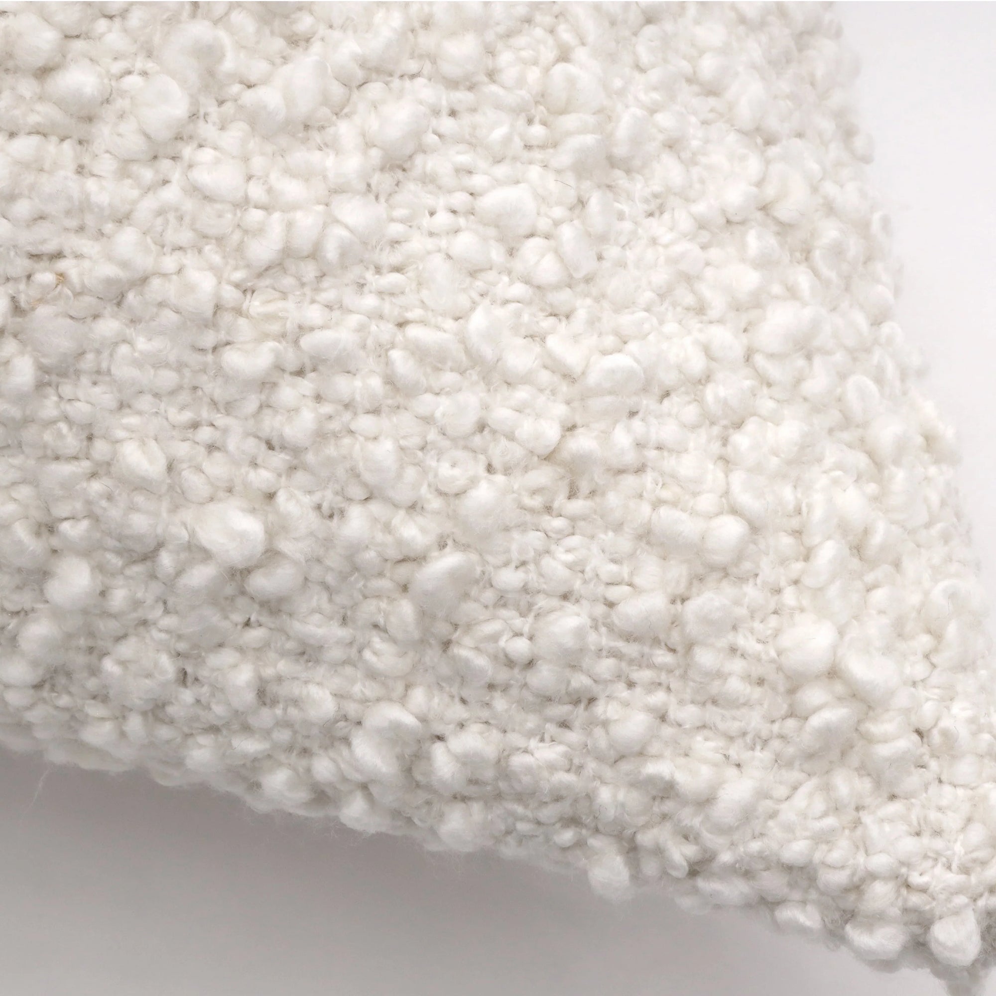 A close-up view of the Murphy Big Pillow 28x36 by POM POM showcases its white, bumpy bouclé texture. The soft, woven textile of this pillow has a plush and cozy appearance, highlighting the intricate detail and craftsmanship of the material. The background is a plain, neutral color.