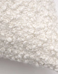 A close-up view of the Murphy Big Pillow 28x36 by POM POM showcases its white, bumpy bouclé texture. The soft, woven textile of this pillow has a plush and cozy appearance, highlighting the intricate detail and craftsmanship of the material. The background is a plain, neutral color.