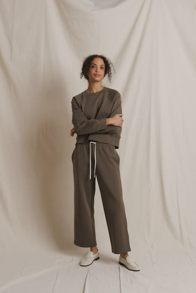 Brown Perfectwhitetee Claud track pant styled with white shoes, shown against a beige draped background.