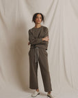 Brown Perfectwhitetee Claud track pant styled with white shoes, shown against a beige draped background.