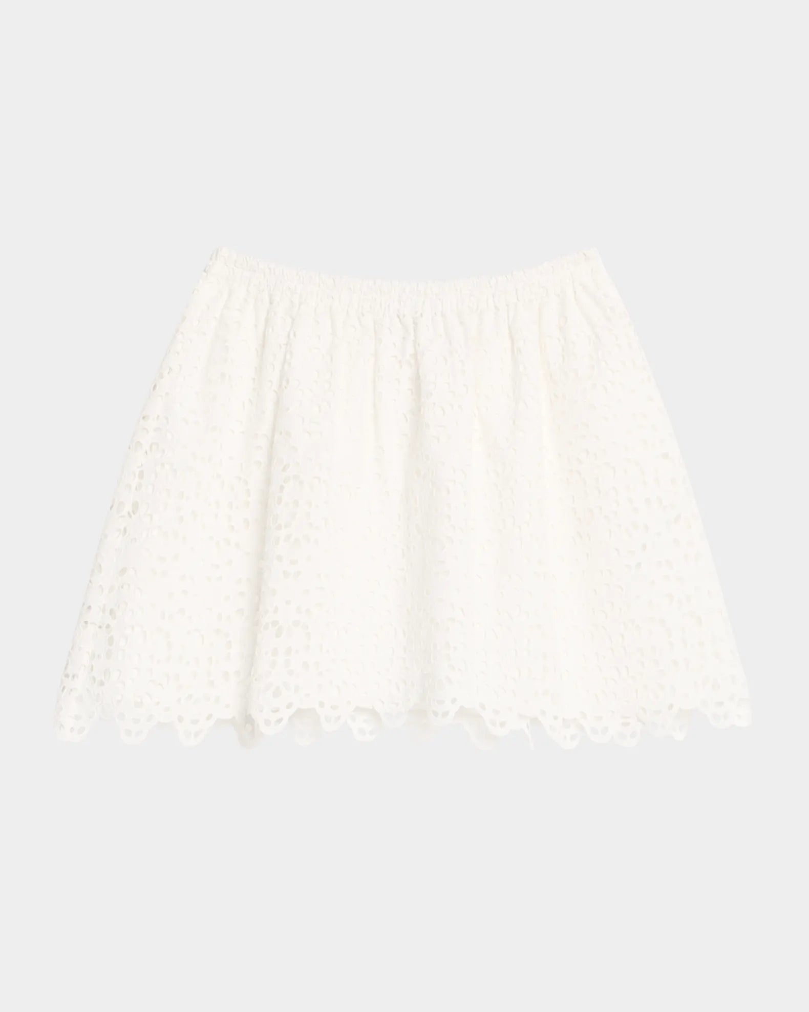 The Deco Eyelet Skirt by FRAME is a white, high-rise cotton skirt with an elastic waistband, scalloped lace hem, and A-line silhouette, shown against a plain light gray background.