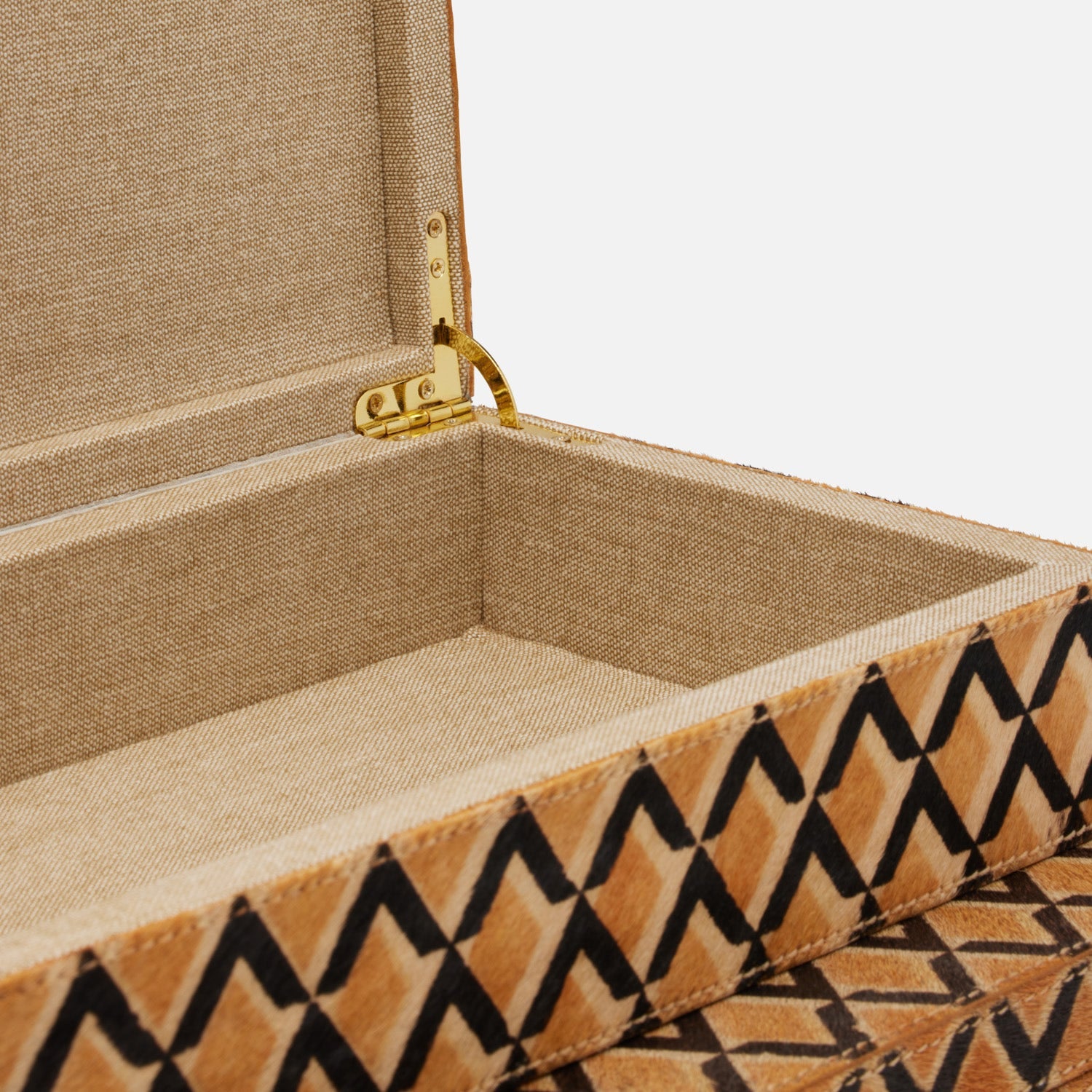 A close-up of the Made Goods Zion Hair on Hide Box, an open rectangular piece lined with beige fabric and gold hinge, showcasing a geometric black zigzag pattern on its exterior.