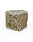 The Marseille Olive Oil Soap by Cie Luxe Brands is a cube-shaped French bar made with botanical oils, featuring embossed French text and a side stamp, all in a muted olive-green color.